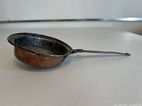 Side view of the vintage small copper pan showing the rounded copper body and iron handle.