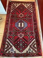 Full view of vintage Persian carpet on floor showing intricate geometric and floral patterns in red, cream, blue, pink, and black tones