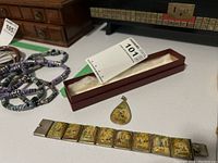 Arabic silver-tone bracelet with rectangular lacquered panels displayed next to matching teardrop pendant on table.