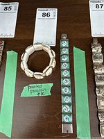 Photo of a painted porcelain tile elasticized bracelet with square tiles showing painted romantic scenes, tag with lot number 86