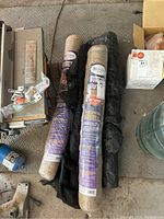 Two rolls of burlap and partial rolls of black plastic tarp and landscape fabric on floor.