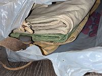 Bags viewed folded inside a plastic bag showing beige, green, and tan canvas materials with leather strap detail