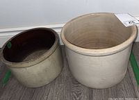 Photo of two vintage stoneware crocks side by side on wooden floor showing size and condition.