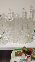 Photo showing assortment of clear crystal glassware including multiple glasses and three decanters with stoppers.