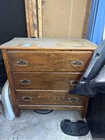 Front view of wood dresser showing three drawers with metal handles, surface shows wear and dirt, used condition.