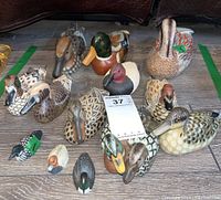 Overall view of 13 carved and hand-painted duck decoys with various colors and sizes, some with visible number tags.