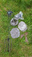 Overall lot items laid out on grass showing two stone bug plaques, stone figurine, metal stakes with bird silhouettes, and small bird toppers.