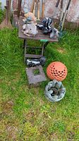 Photo of all items on and around the folding plastic table placed outdoors including stone and resin lawn ornaments, lantern, and ornate ball.