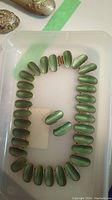 Top view of necklace and earrings arranged in a tray showing greenish brushed silver elongate ovals.