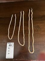 Three knotted pearl necklaces of different lengths (18.5, 24, 30 inches) displayed on a wooden surface with a label showing lengths.
