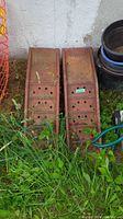 Pair of rusted metal ramps placed on grass leaning against a white wall