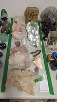 Wide view of table showing various rocks, minerals, carved bookends, colorful glass marbles, paperweights, a large druzy, rose quartz, amethyst and shells.