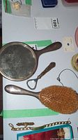 Photo showing the front of the hand mirror, bottle opener, and hairbrush lying on a table with other small items nearby.