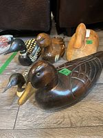 Front angle of five wooden waterfowl carvings including two loons and three ducks with various painted and natural finishes on a wooden floor.