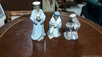 Set of three ceramic wise men on wooden surface, showing the trio clearly with standing and kneeling positions