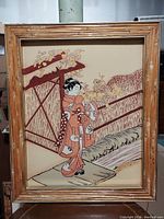 Full view of the framed large Asian-inspired artwork depicting a woman in traditional attire on a porch, with a bamboo and gold frame.
