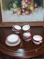 Full set of Limoges Mandarin Maroon china arranged on a table, showing all items including teacups, saucers, dessert bowls, creamer, and sugar bowl.