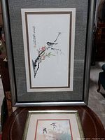 Frontal view of both framed Asian inspired bird prints, showing large watercolor print with gray fabric matting and smaller print with beige matting.