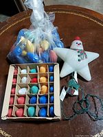 Vintage C9 Christmas bulbs in a box with assorted colors and a bag of bulbs along with a snowman star shaped tree topper on a wooden surface.
