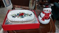Platter and snowman cookie jar side by side on table with cards and chairs in background