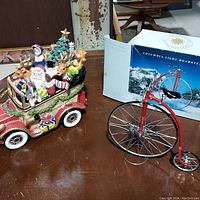 Photo showing the Fitz and Floyd ceramic Christmas music box car with Santa Claus, reindeer, and other holiday figures alongside the Columbia Light Roadster unicycle decor and its original box.