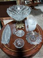Overview of the large cut glass bowl on gold metal base, with the smaller cut glass candy/fruit dishes and kidney-shaped dishes arranged on wooden round table.