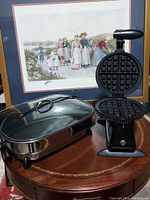 Photo of GE stainless steel electric skillet with glass lid and black GE waffle maker with open top showing waffle grids.