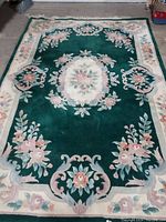 Top view of entire green floral wool area rug showing central and border floral patterns and condition.