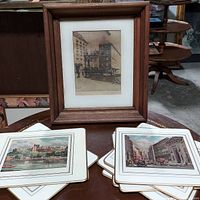 Wood framed etching showing a street scene with buildings, signed by artist, matted, in simple wooden frame. Array of cork-backed landmark boards displayed below the framed etching.