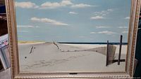Front view of the large framed beach artwork showing sand dunes, wooden fence, ocean, sky with clouds, and part of the gold frame.