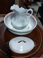 Large white ceramic pitcher with embossed floral details inside a large serving bowl with floral patterns.