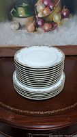 Stack of white porcelain plates with gold decorative rim, including five dinner plates and eleven salad plates.