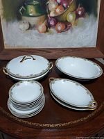 Photo showing all porcelain pieces: 1 large covered serving bowl, 1 large serving bowl, 2 medium serving bowls, 3 saucers, 3 dessert bowls, all with white base and gold decorative trim and handles on some pieces