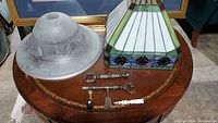 Frosted globe lamp shade and Tiffany-style stained glass lamp shade on table with finials.