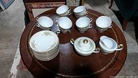 PB China tea set including sugar bowl with lid, creamer, 12 teacups, and 12 saucers displayed on a wooden round table.