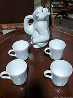 Photo showing the polar bear pitcher and four pink rimmed mugs arranged on a round table with a rusty metal surface.