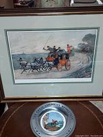 Silver-tone commemorative plate with blue lettering around the rim and painted scene of rider near a building.