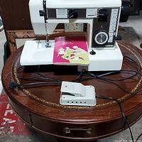 Front view of Brother sewing machine with power cord, foot pedal, and sewing instruction booklet on table.
