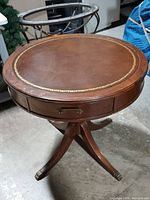 Top and leg view showing round wooden table with gold border on top, pull out drawer with gold handles, and claw metal feet on legs