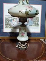 Front and side view of vintage glass globe lamp showing floral painted designs on light green tinted glass shade and base, cord coiled at bottom