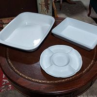 Three white ceramic dishes on round wooden tabletop: large casserole, rectangular baking dish, divided serving dish.