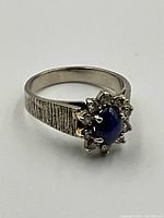 Front view of ring showing textured band and central blue gemstone surrounded by diamonds