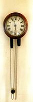 Clock hanging on wall showing full front view with wood case, chains, weights and pendulum bob