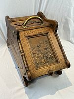 Three-quarter front view showing oak construction, curved top and brass relief panel