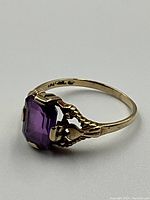 Three-quarter side view showing emerald-cut amethyst in filigree prong setting