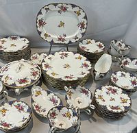 Full layout of cups, saucers, plates, bowls, and serving pieces against neutral backdrop.