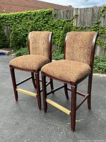 Pair of bar stools side by side outdoors on asphalt with wooden fence background