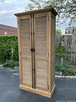 Front three-quarter view of tall oak cabinet showing louvered doors, crown molding and base molding