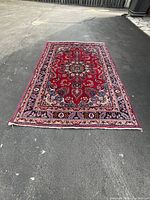 Full view of red hand knotted area rug laid on asphalt