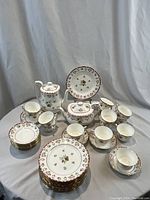 Overview of entire set arranged on draped cloth, shows plates, cups, saucers, tea pots, sugar bowl and creamer